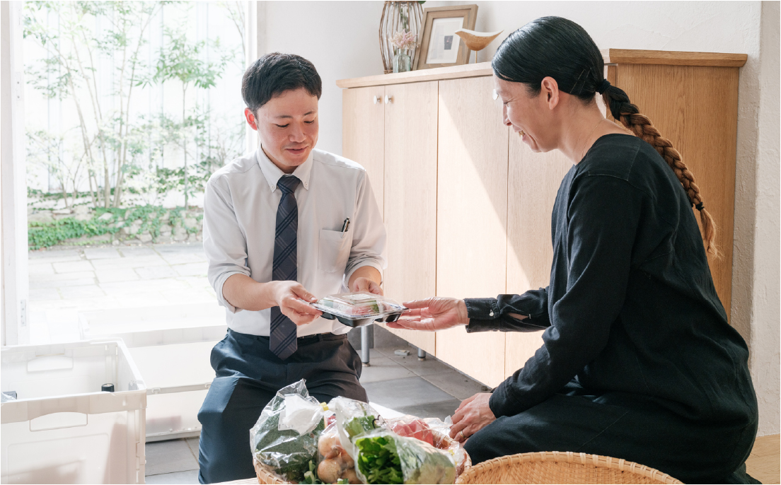 玄関先で、会員のお客様に旬の食材を手渡す専属スタッフ